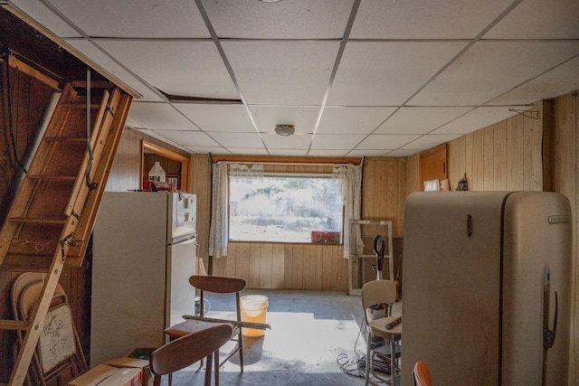 interior space featuring a paneled ceiling, wooden walls, and white fridge