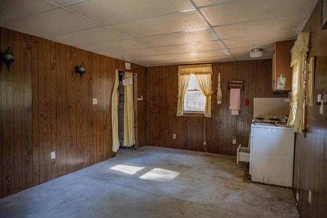 empty room featuring a drop ceiling, concrete flooring, and wooden walls