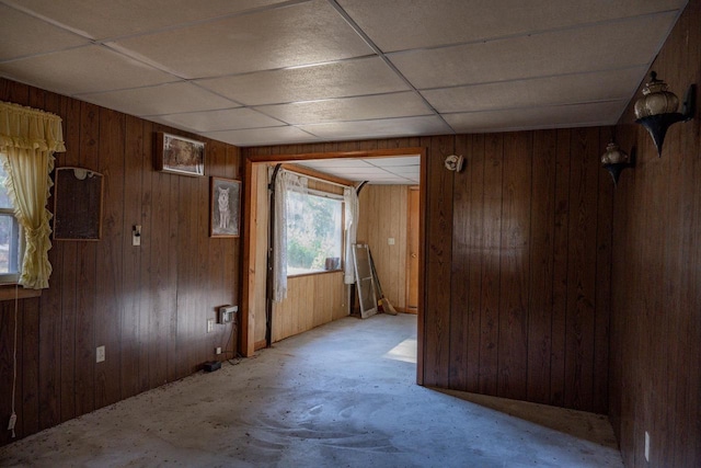 unfurnished room featuring wooden walls and a drop ceiling