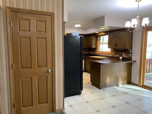 kitchen with black refrigerator, a notable chandelier, sink, backsplash, and decorative light fixtures