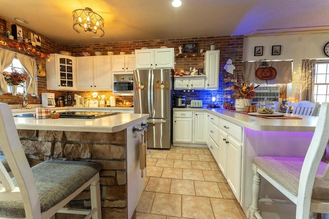 kitchen with a kitchen bar, stainless steel appliances, brick wall, and white cabinets