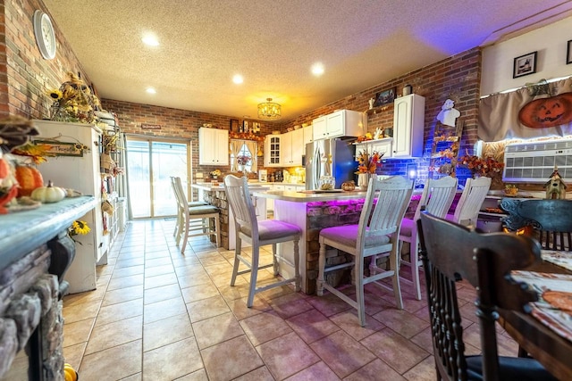 kitchen featuring white cabinets, a kitchen bar, stainless steel refrigerator, and brick wall