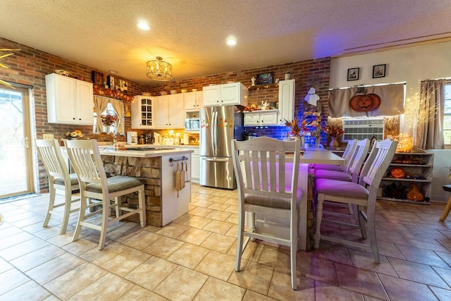 kitchen featuring white cabinets, a textured ceiling, an island with sink, appliances with stainless steel finishes, and brick wall