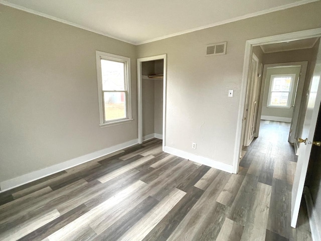 unfurnished bedroom with a closet, multiple windows, dark hardwood / wood-style floors, and crown molding