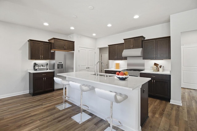 kitchen with appliances with stainless steel finishes, a breakfast bar, a kitchen island with sink, dark wood-type flooring, and sink