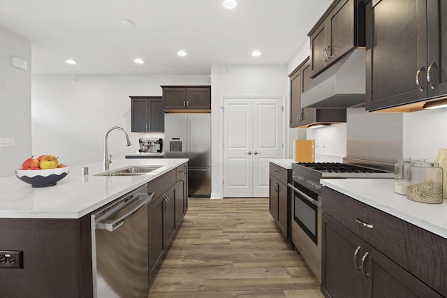 kitchen featuring dark brown cabinetry, sink, light hardwood / wood-style flooring, an island with sink, and appliances with stainless steel finishes