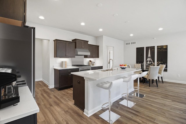 kitchen featuring sink, a kitchen island with sink, a breakfast bar, appliances with stainless steel finishes, and light wood-type flooring