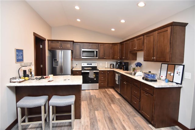 kitchen with appliances with stainless steel finishes, vaulted ceiling, dark brown cabinets, and light hardwood / wood-style floors