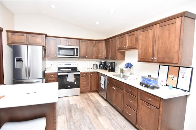 kitchen featuring appliances with stainless steel finishes, lofted ceiling, sink, and light hardwood / wood-style flooring