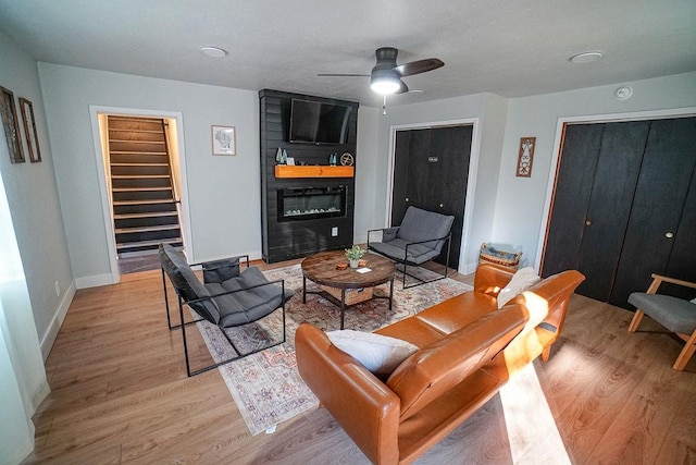 living room with a large fireplace, light hardwood / wood-style floors, and ceiling fan