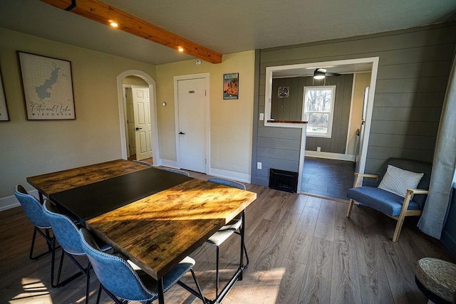 dining room featuring a large fireplace, beamed ceiling, wood-type flooring, and ceiling fan