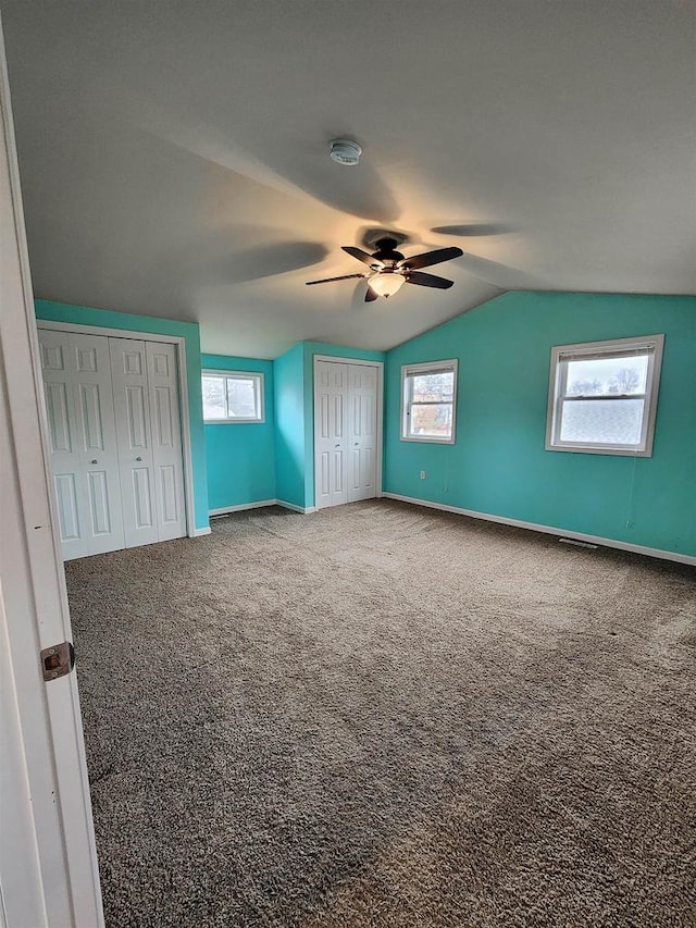 unfurnished bedroom featuring multiple windows, lofted ceiling, ceiling fan, and carpet