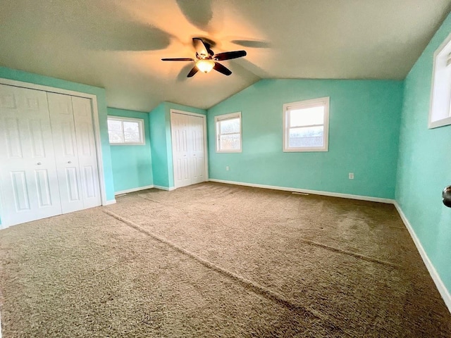 unfurnished bedroom with ceiling fan, multiple closets, lofted ceiling, and carpet floors