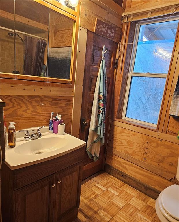 bathroom featuring toilet, wood walls, vanity, walk in shower, and parquet flooring