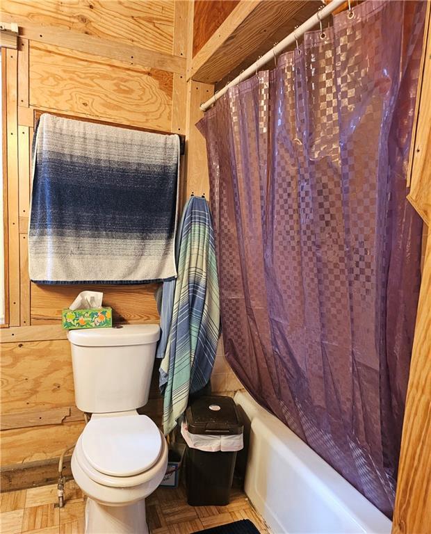 bathroom featuring shower / bath combo with shower curtain, parquet floors, toilet, and wooden walls