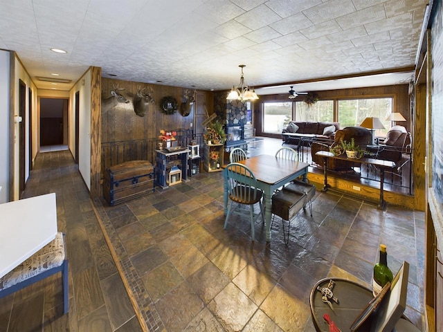 dining room with ceiling fan with notable chandelier and wood walls