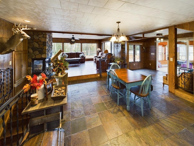 dining area featuring wooden walls, ceiling fan with notable chandelier, and a fireplace