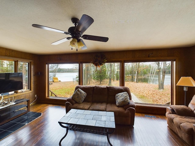 living room featuring a water view, wooden walls, hardwood / wood-style flooring, and ceiling fan