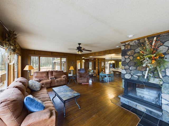 living room with ceiling fan, dark hardwood / wood-style floors, a textured ceiling, a stone fireplace, and wooden walls