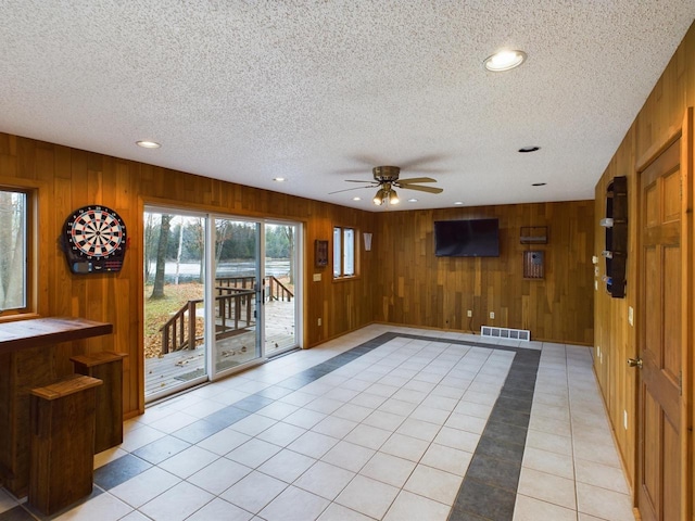 interior space with wood walls, a textured ceiling, ceiling fan, and light tile patterned flooring