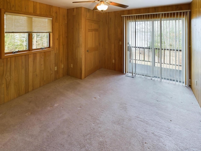 carpeted spare room with wooden walls and ceiling fan