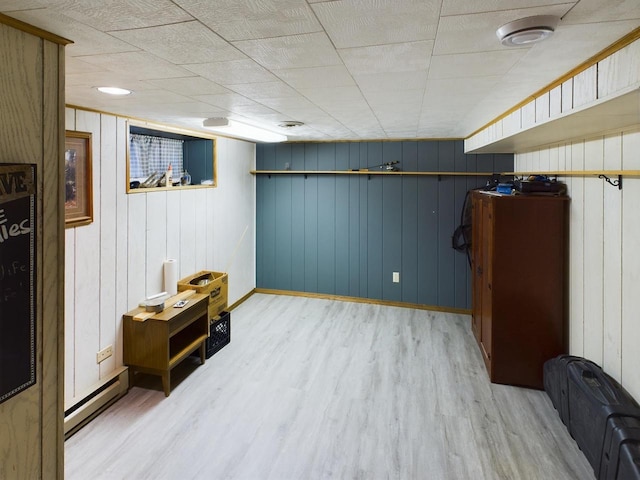 basement with wood walls, baseboard heating, and light hardwood / wood-style floors