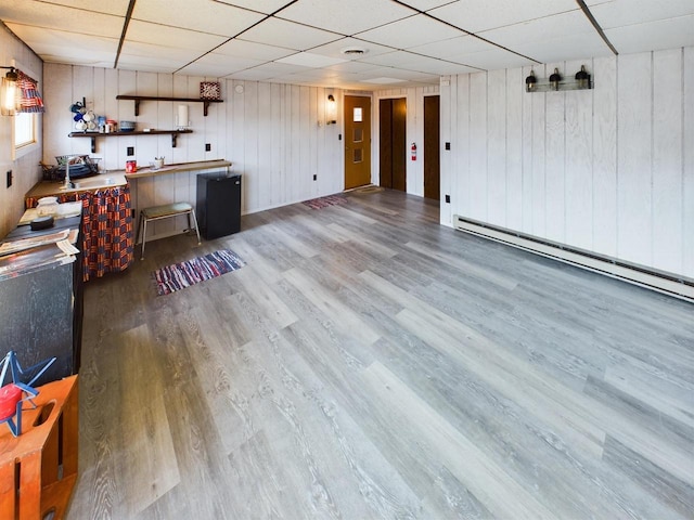 interior space featuring wood walls, a drop ceiling, hardwood / wood-style flooring, and a baseboard radiator