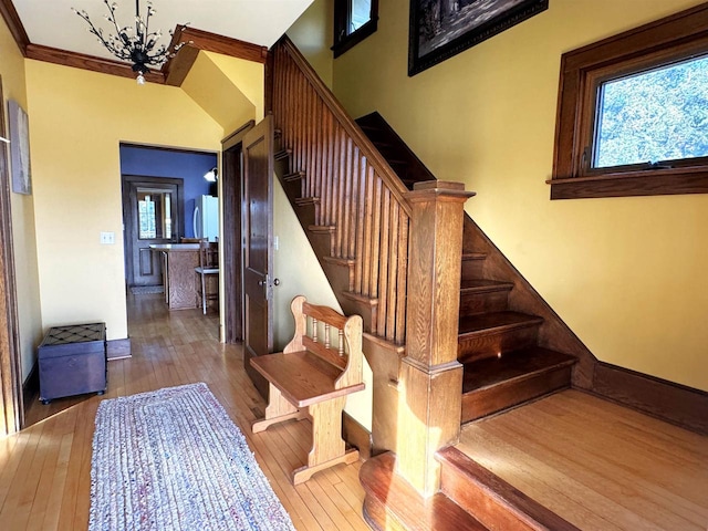 stairway with a chandelier, wood-type flooring, and ornamental molding