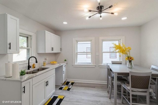 kitchen with light wood-type flooring, sink, stainless steel dishwasher, and white cabinets