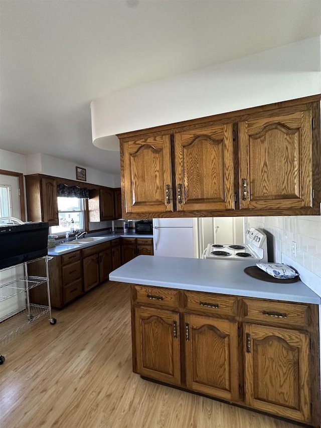 kitchen with light wood-type flooring, decorative backsplash, kitchen peninsula, and white appliances