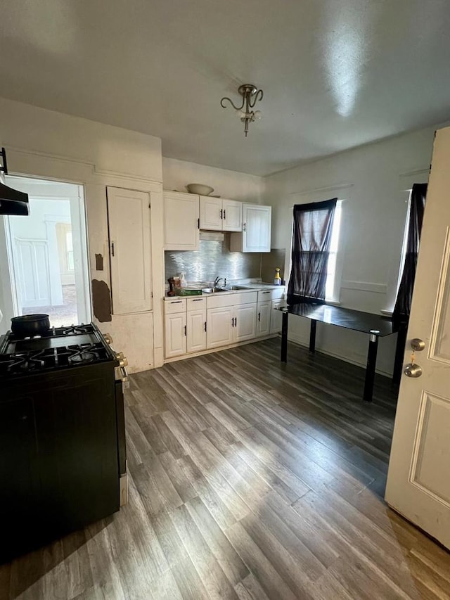 kitchen with gas stove, backsplash, hardwood / wood-style flooring, and white cabinets