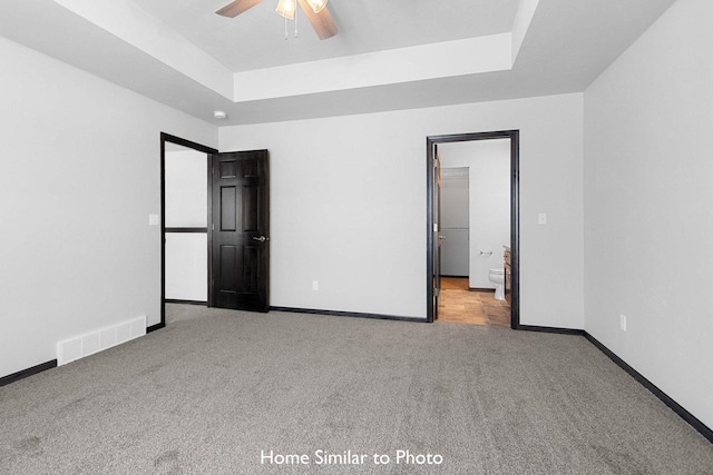 unfurnished bedroom featuring ceiling fan, a raised ceiling, light carpet, and a walk in closet