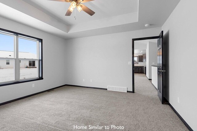 empty room with light carpet, a raised ceiling, and ceiling fan