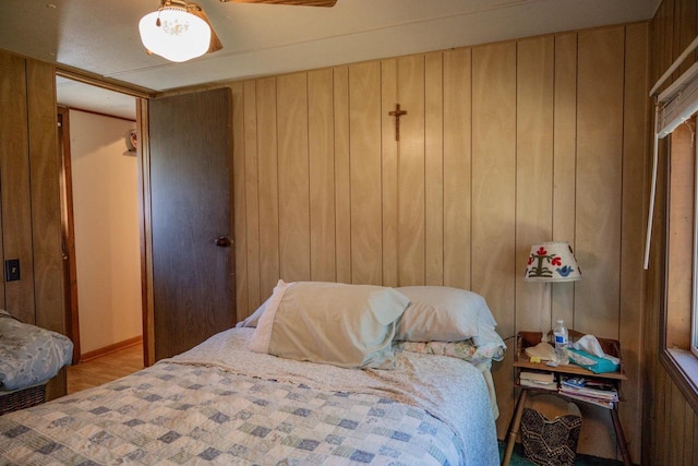 bedroom with ceiling fan, wood walls, and light wood-type flooring