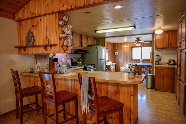 kitchen with light hardwood / wood-style flooring, kitchen peninsula, a breakfast bar area, exhaust hood, and appliances with stainless steel finishes