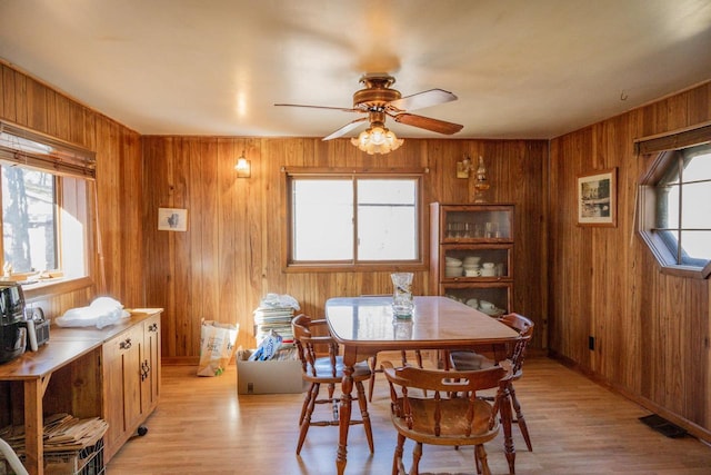 dining room with wood walls, ceiling fan, and light hardwood / wood-style floors