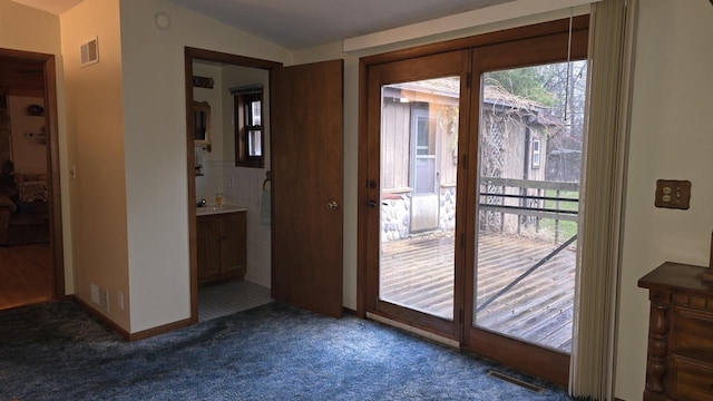 entryway featuring vaulted ceiling, dark carpet, and a healthy amount of sunlight