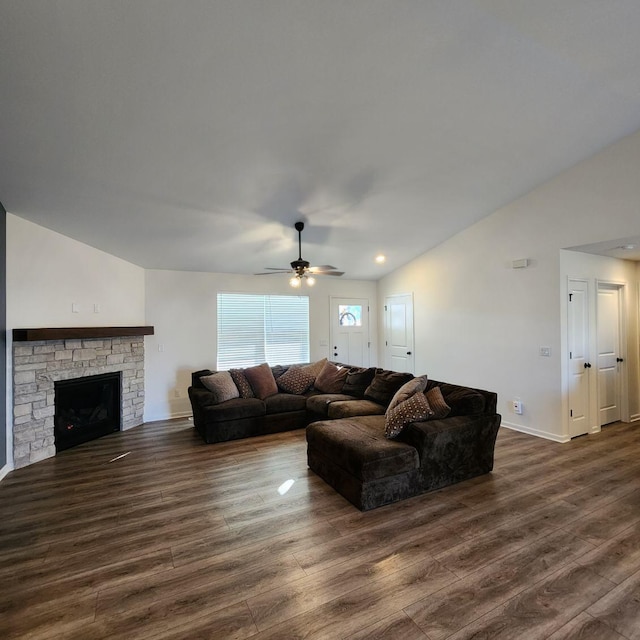 living room with dark hardwood / wood-style flooring, vaulted ceiling, ceiling fan, and a stone fireplace