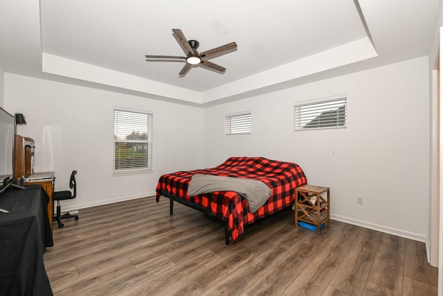 bedroom with a raised ceiling, ceiling fan, and dark wood-type flooring