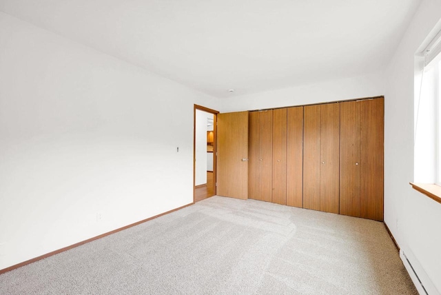 unfurnished bedroom featuring a baseboard radiator, light carpet, and a closet