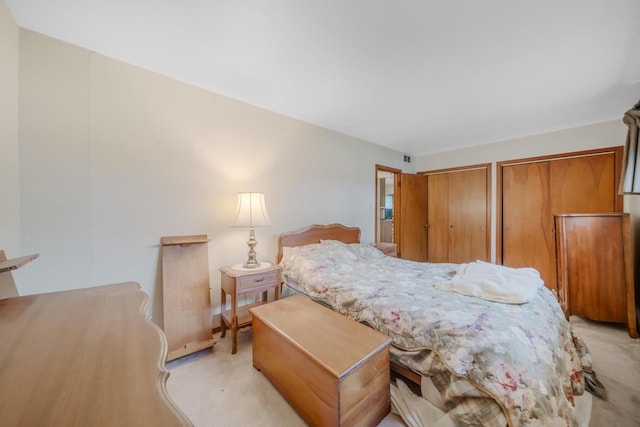 bedroom with light colored carpet and two closets