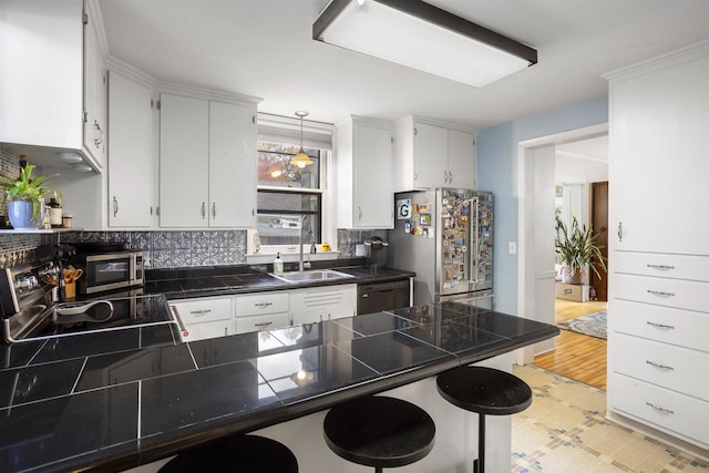 kitchen with stainless steel appliances, white cabinetry, hanging light fixtures, sink, and light hardwood / wood-style floors