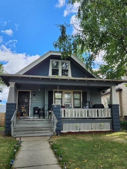 bungalow-style home with a front lawn, cooling unit, and covered porch