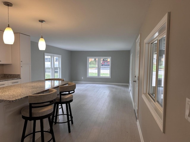 kitchen with white cabinetry, a kitchen bar, stone countertops, hanging light fixtures, and light hardwood / wood-style floors