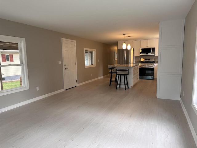 kitchen featuring stainless steel appliances, a center island, white cabinets, a breakfast bar, and decorative light fixtures