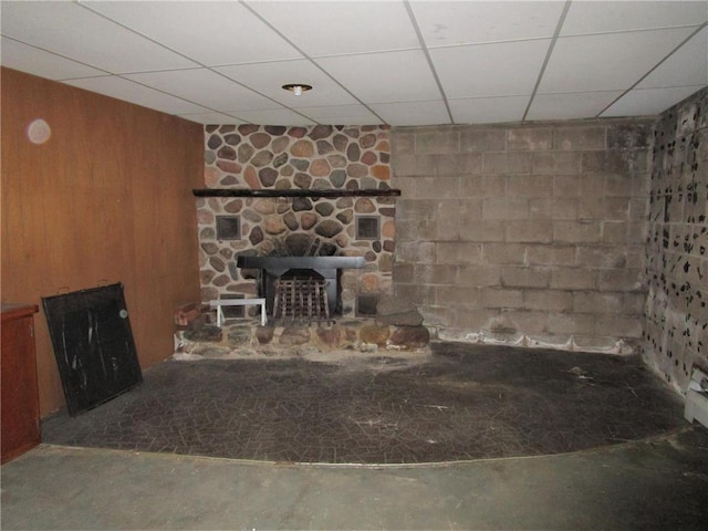 unfurnished living room with a stone fireplace, wood walls, a drop ceiling, and concrete flooring