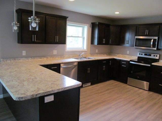 kitchen featuring sink, kitchen peninsula, appliances with stainless steel finishes, decorative light fixtures, and light hardwood / wood-style flooring