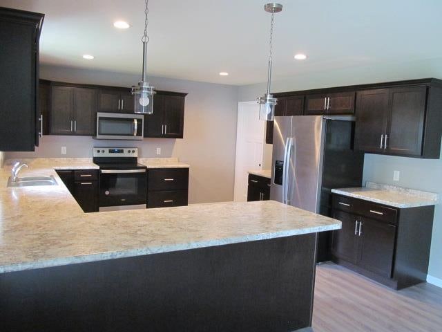 kitchen featuring pendant lighting, appliances with stainless steel finishes, sink, and light hardwood / wood-style flooring