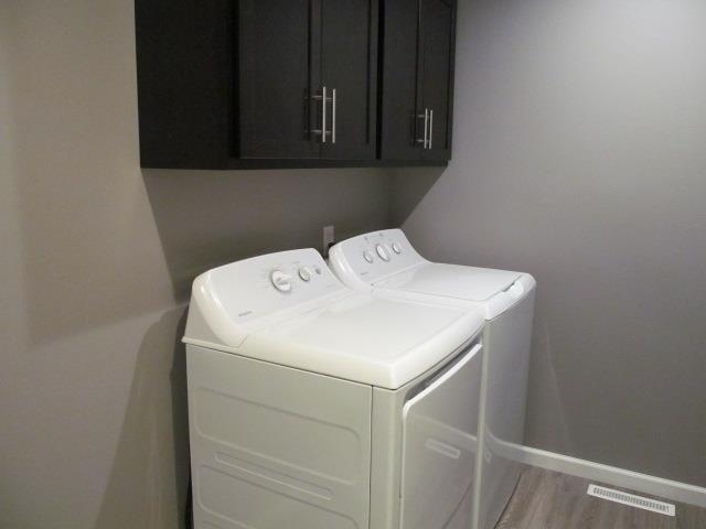 clothes washing area with light hardwood / wood-style flooring, washing machine and dryer, and cabinets