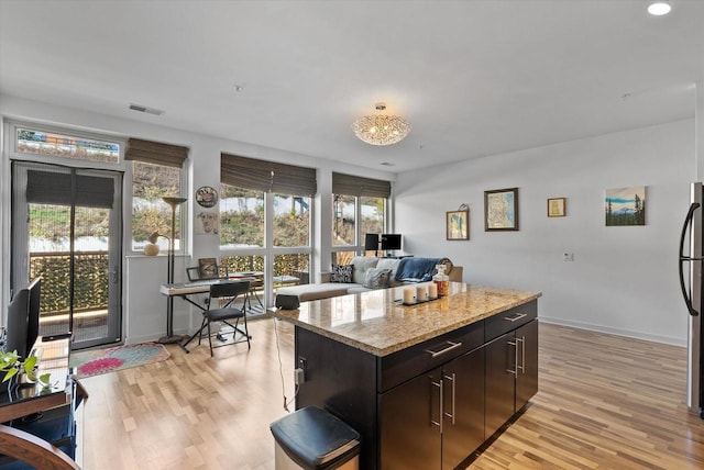 kitchen with dark brown cabinetry, a kitchen island, light stone countertops, light hardwood / wood-style flooring, and stainless steel fridge